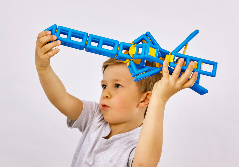 Child holding a blue and yellow toy structure above their head against a white background